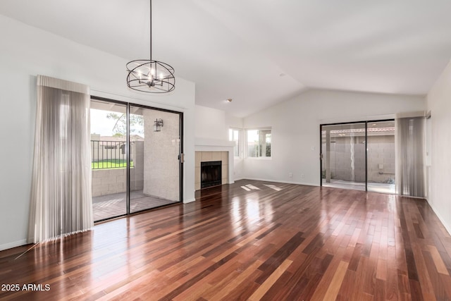 unfurnished living room with a healthy amount of sunlight, vaulted ceiling, wood finished floors, and a tile fireplace