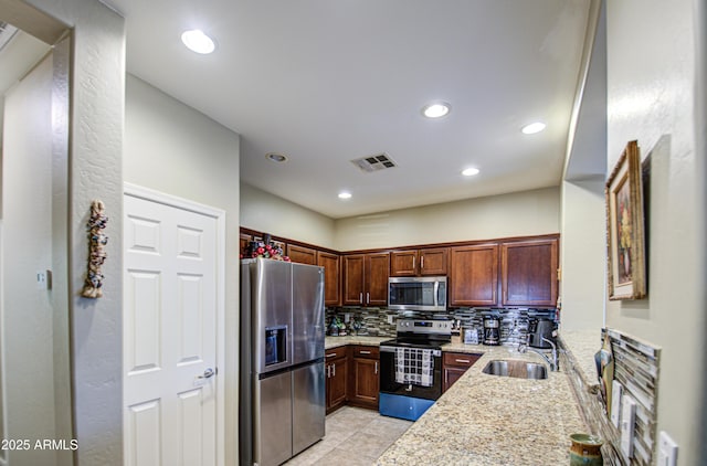 kitchen with sink, light tile patterned floors, appliances with stainless steel finishes, light stone countertops, and decorative backsplash