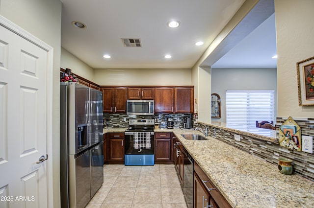 kitchen featuring sink, light stone counters, appliances with stainless steel finishes, kitchen peninsula, and backsplash