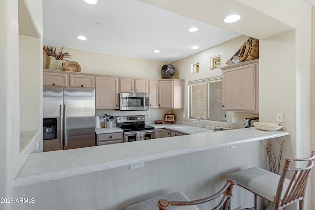 kitchen featuring light brown cabinetry, recessed lighting, a peninsula, stainless steel appliances, and a sink