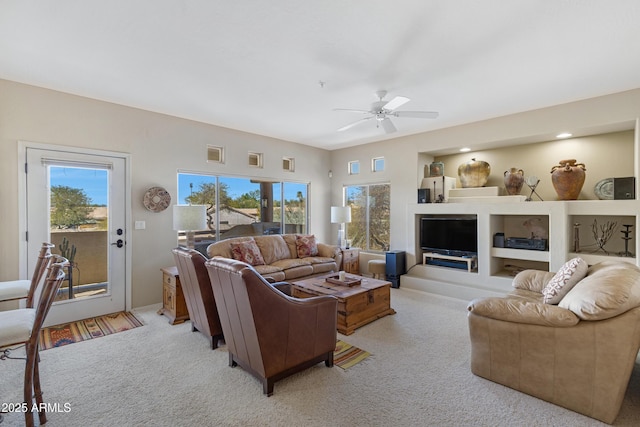 living area with built in shelves, light colored carpet, and ceiling fan