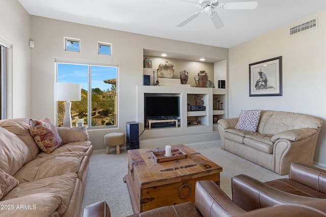 carpeted living area featuring built in shelves, baseboards, visible vents, and ceiling fan