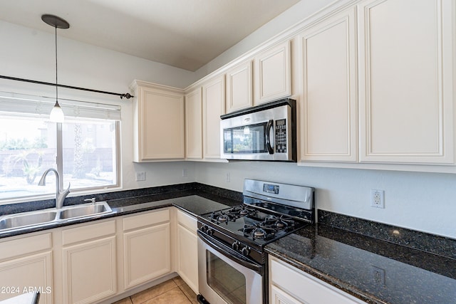 kitchen featuring dark stone countertops, light tile patterned flooring, stainless steel appliances, decorative light fixtures, and sink