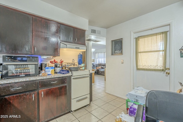 kitchen featuring under cabinet range hood, light tile patterned floors, visible vents, and gas range gas stove