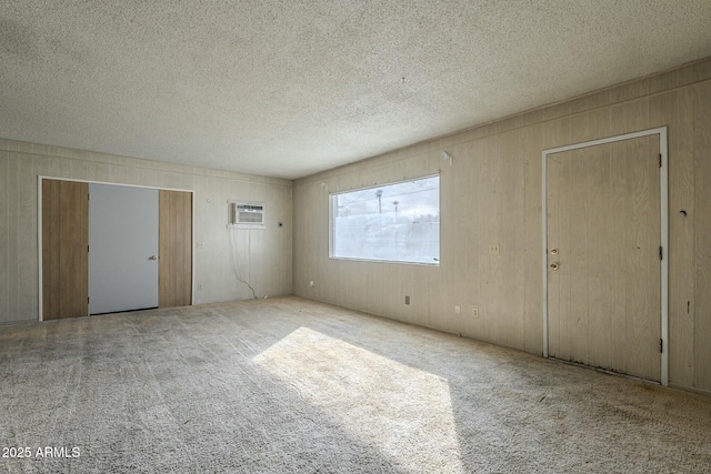 empty room with a textured ceiling, wood walls, carpet, and a wall unit AC