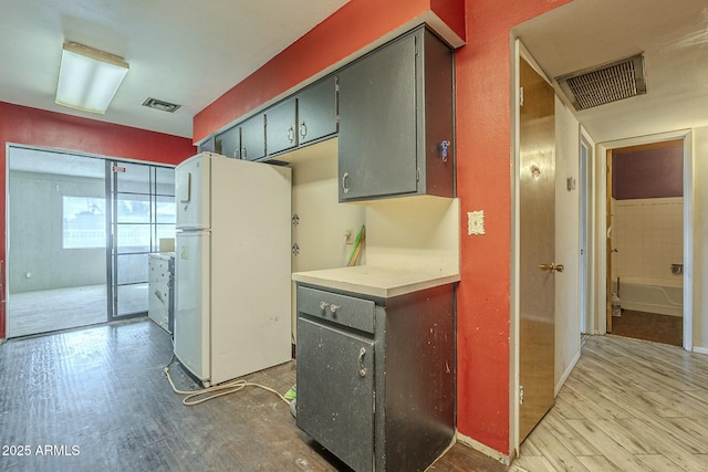 kitchen with light countertops, freestanding refrigerator, visible vents, and wood finished floors