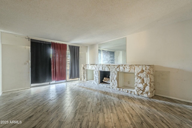 unfurnished living room featuring a textured ceiling, a fireplace, baseboards, and wood finished floors