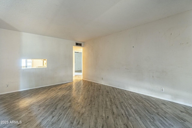 empty room with a textured ceiling, visible vents, and wood finished floors