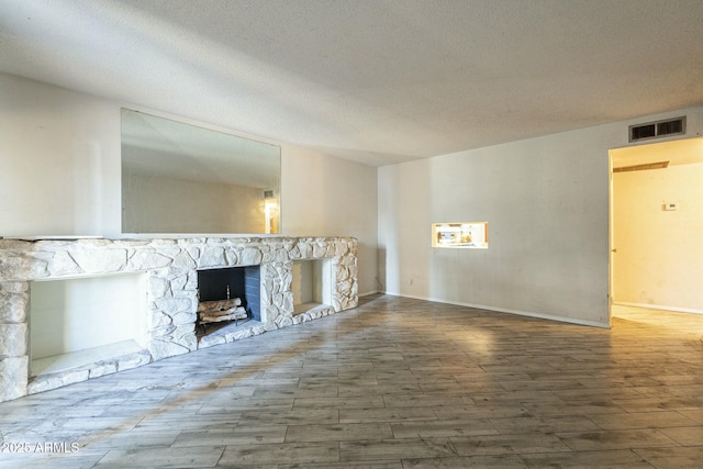 unfurnished living room with visible vents, a stone fireplace, a textured ceiling, and wood finished floors