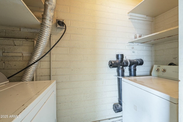 laundry area with laundry area, brick wall, and washer and dryer