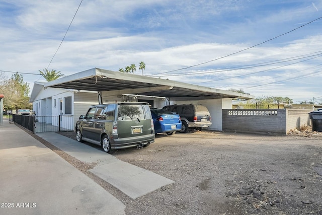 view of vehicle parking featuring driveway, fence, and a carport