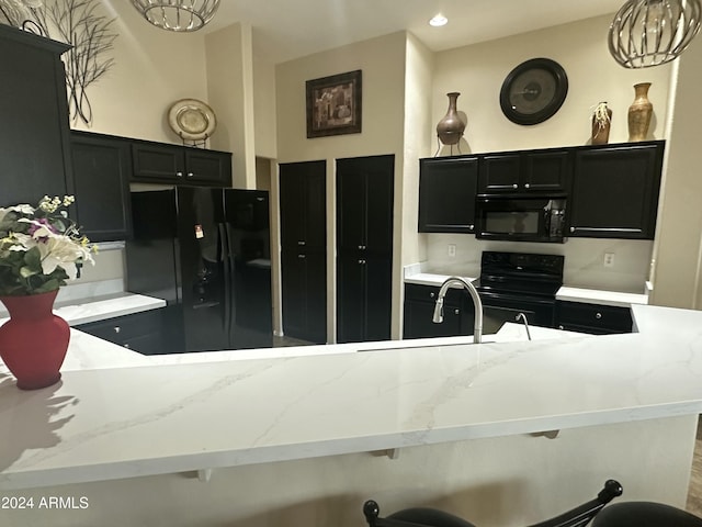 kitchen featuring light stone counters, an inviting chandelier, a breakfast bar area, and black appliances