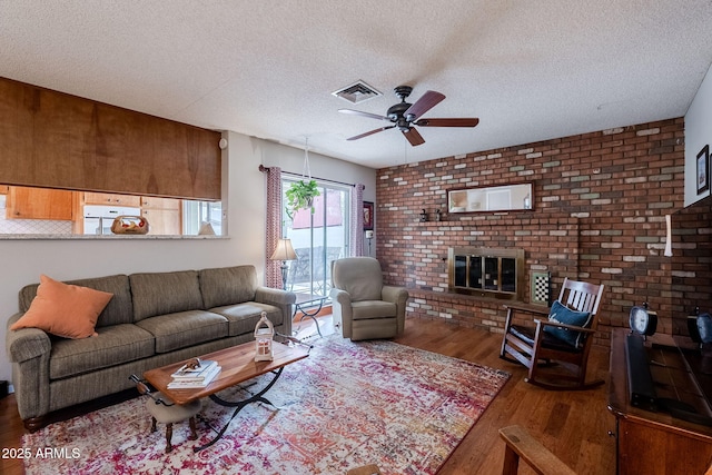 living room with a brick fireplace, hardwood / wood-style flooring, a textured ceiling, and ceiling fan