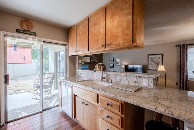 kitchen with sink, light stone counters, light wood-type flooring, dishwasher, and kitchen peninsula