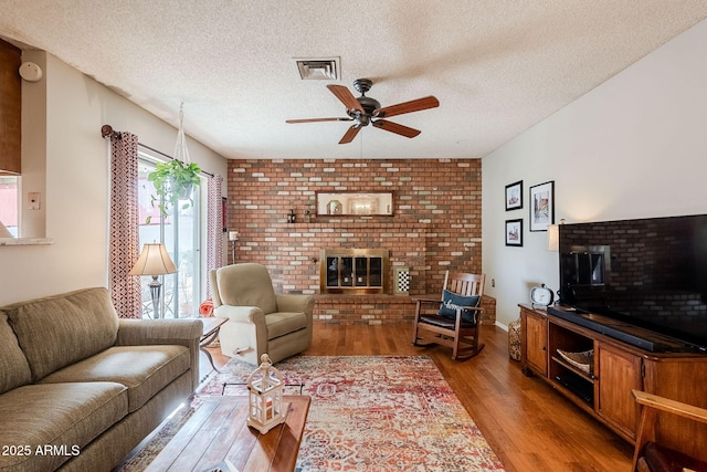 living room featuring hardwood / wood-style flooring, ceiling fan, a fireplace, and a textured ceiling