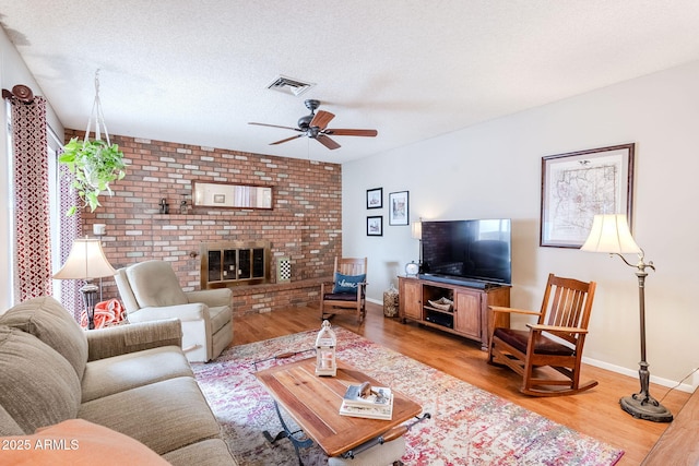 living room featuring ceiling fan, a brick fireplace, hardwood / wood-style floors, and a textured ceiling