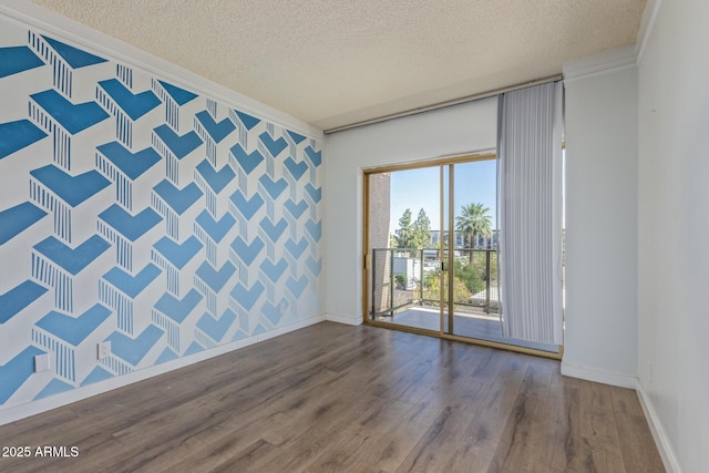 unfurnished room featuring wallpapered walls, a textured ceiling, wood finished floors, crown molding, and an accent wall