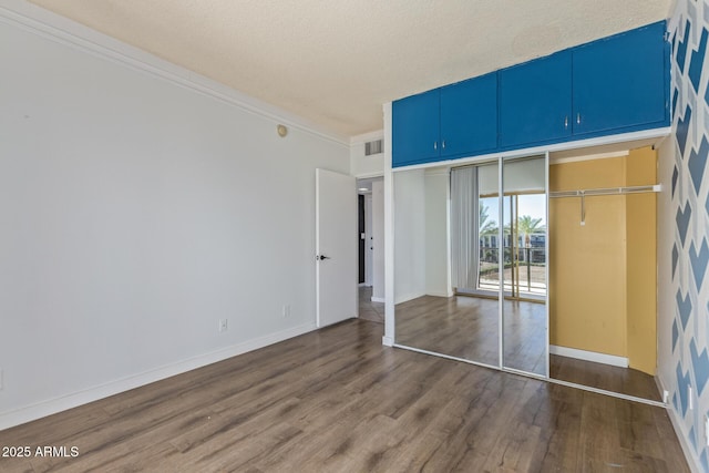 unfurnished bedroom with dark wood-style flooring, a closet, a textured ceiling, baseboards, and crown molding