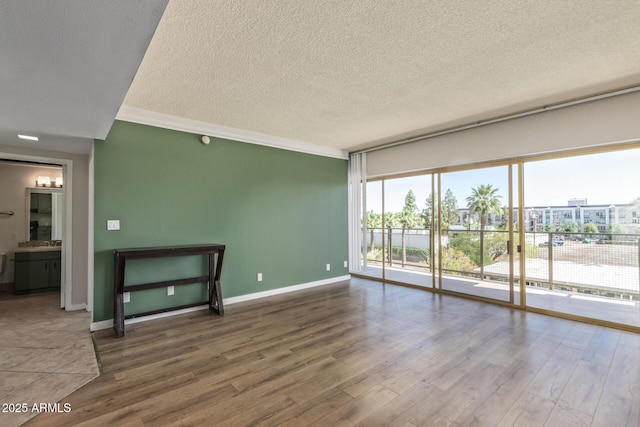 unfurnished room with a textured ceiling, wood finished floors, and baseboards