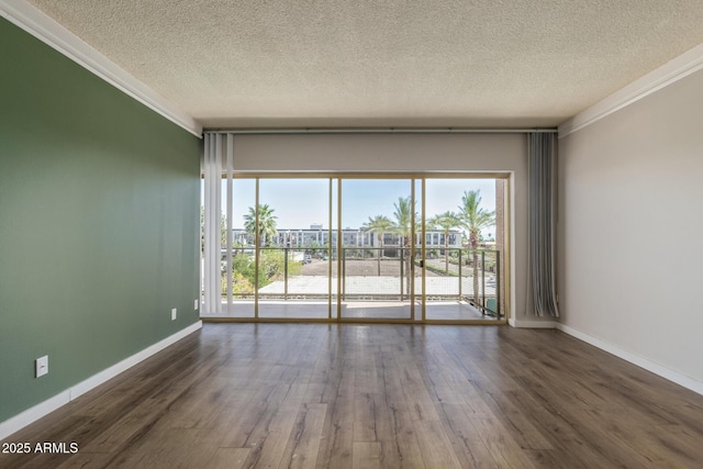 spare room with a textured ceiling, ornamental molding, wood finished floors, and baseboards
