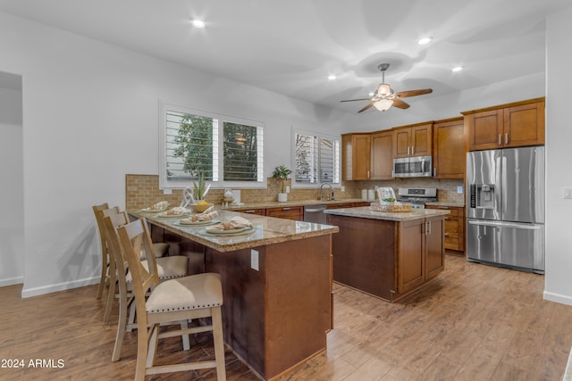 kitchen featuring light wood-type flooring, tasteful backsplash, stainless steel appliances, a center island, and light stone countertops