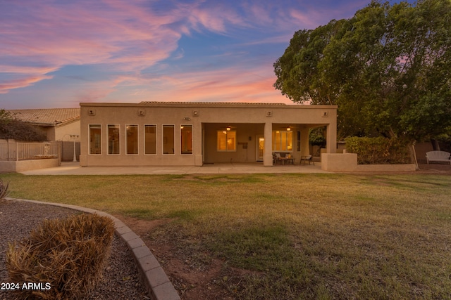 back house at dusk with a lawn and a patio