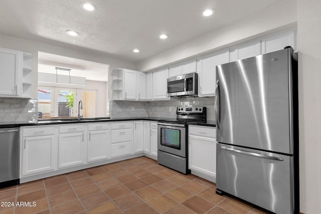 kitchen featuring appliances with stainless steel finishes, backsplash, sink, dark tile patterned flooring, and white cabinetry