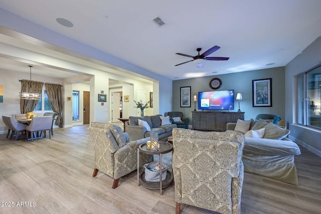 living area featuring light wood-style floors, a ceiling fan, visible vents, and baseboards