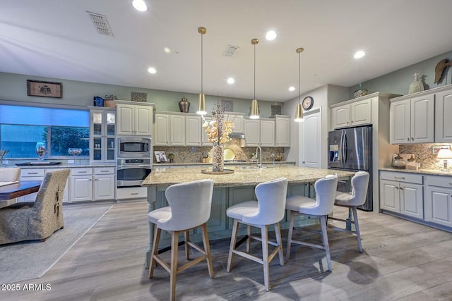 kitchen with light wood-style floors, visible vents, a center island with sink, and appliances with stainless steel finishes