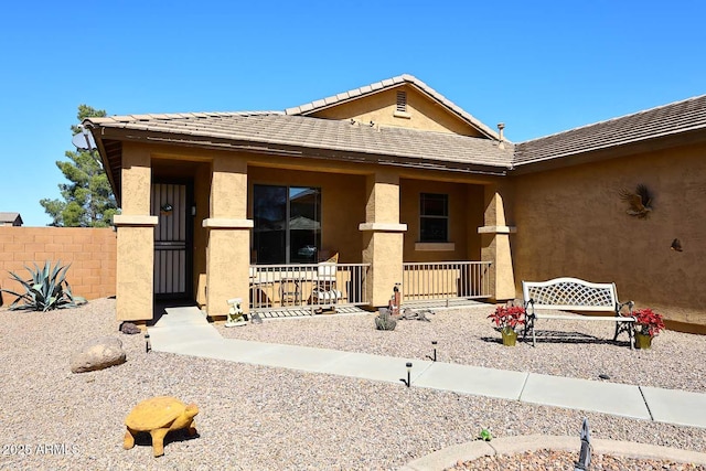 exterior space with a porch, fence, a tiled roof, and stucco siding