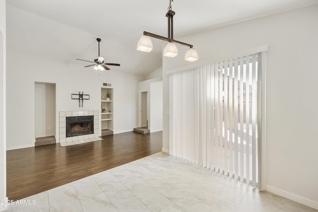 living room featuring lofted ceiling, a tile fireplace, hardwood / wood-style flooring, built in shelves, and ceiling fan