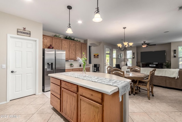 kitchen with stainless steel fridge, ceiling fan with notable chandelier, decorative light fixtures, a kitchen island, and light tile patterned flooring