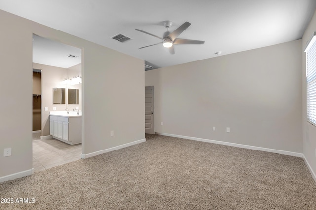 spare room featuring light colored carpet, a sink, a ceiling fan, baseboards, and visible vents