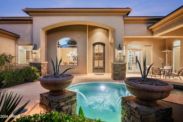 pool at dusk featuring a patio area, pool water feature, and french doors