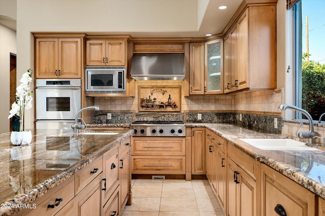 kitchen with wall chimney range hood, appliances with stainless steel finishes, stone counters, and sink