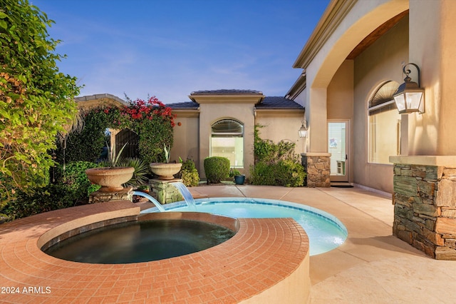 pool at dusk featuring an in ground hot tub and pool water feature