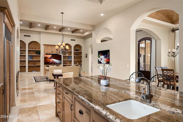 kitchen featuring sink, hanging light fixtures, dark stone countertops, built in features, and a chandelier