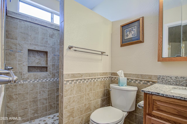 bathroom with tile walls, vanity, toilet, and a tile shower