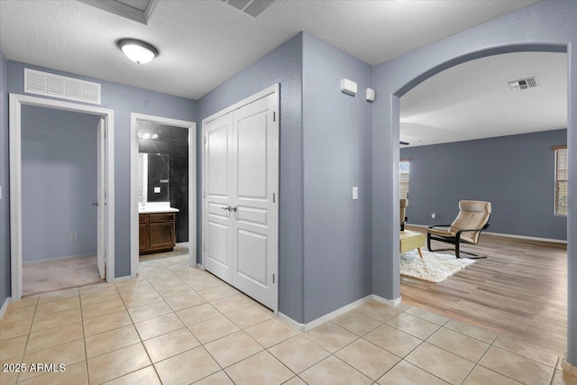 hallway featuring arched walkways, visible vents, and light tile patterned floors