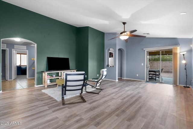 living area with arched walkways, lofted ceiling, ceiling fan, wood finished floors, and baseboards