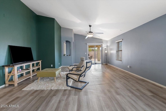 living area featuring a ceiling fan, baseboards, vaulted ceiling, and wood finished floors