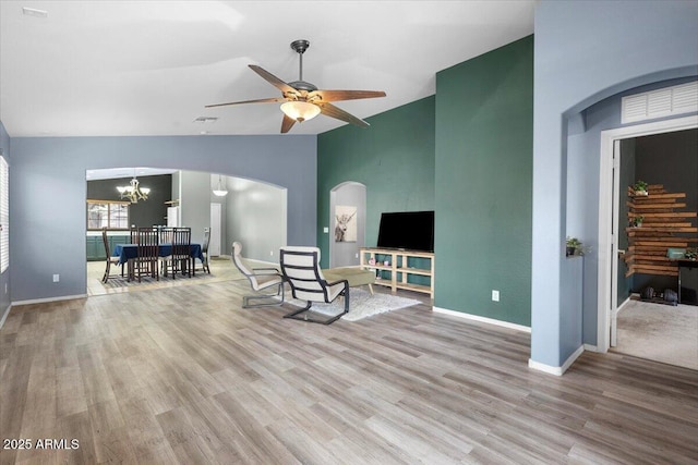 living area featuring baseboards, vaulted ceiling, wood finished floors, and ceiling fan with notable chandelier