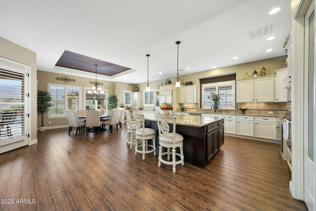 kitchen featuring visible vents, a kitchen island, dark wood-style flooring, a tray ceiling, and backsplash