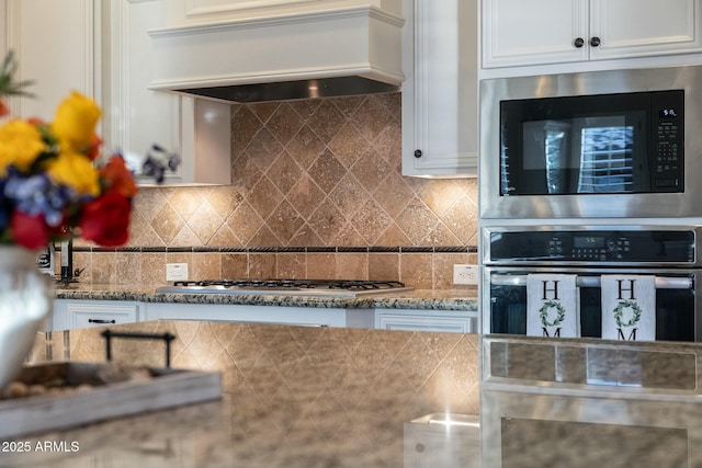 kitchen featuring appliances with stainless steel finishes, white cabinets, custom range hood, and decorative backsplash