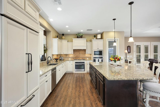 kitchen featuring built in appliances, a breakfast bar area, a sink, and visible vents