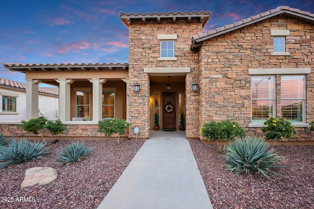 exterior entry at dusk featuring stone siding and a tile roof