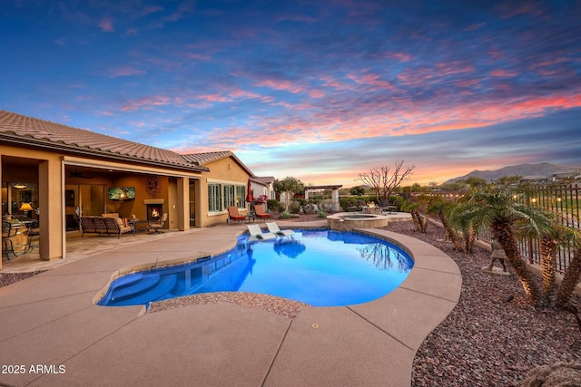 pool at dusk featuring a patio area, a pool with connected hot tub, fence, and an outdoor living space