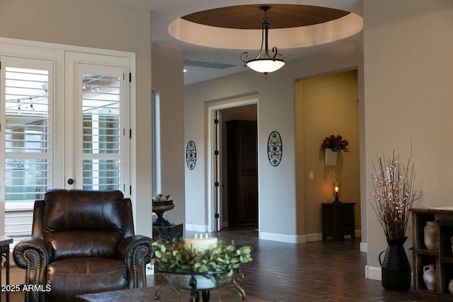 living area featuring visible vents, a tray ceiling, dark wood finished floors, and baseboards