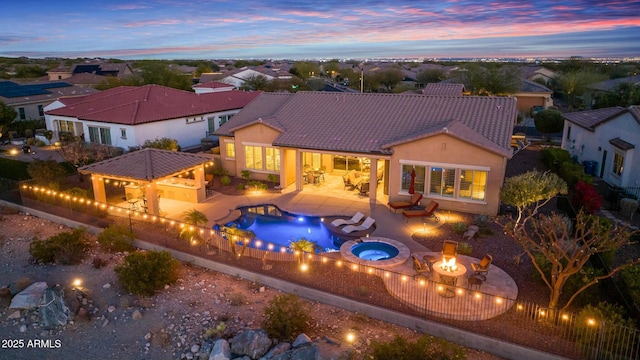 back of property at dusk with outdoor dry bar, stucco siding, a patio area, a fire pit, and a tiled roof