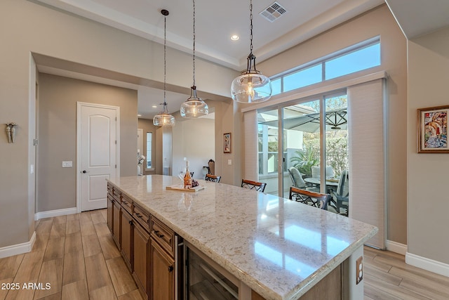 kitchen with light stone counters, a center island, hanging light fixtures, and wine cooler